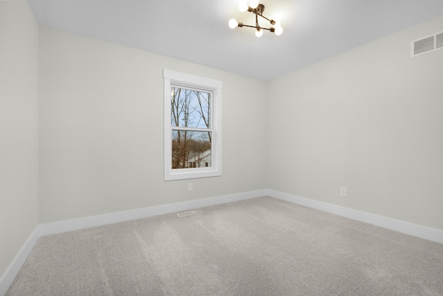 spare room featuring carpet flooring and a notable chandelier