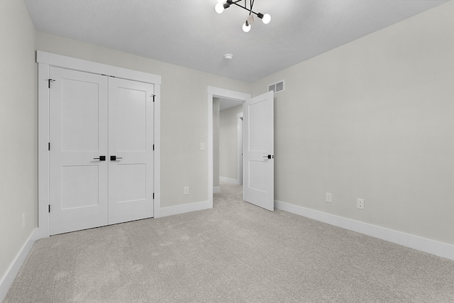 unfurnished bedroom featuring light colored carpet, a closet, and a notable chandelier