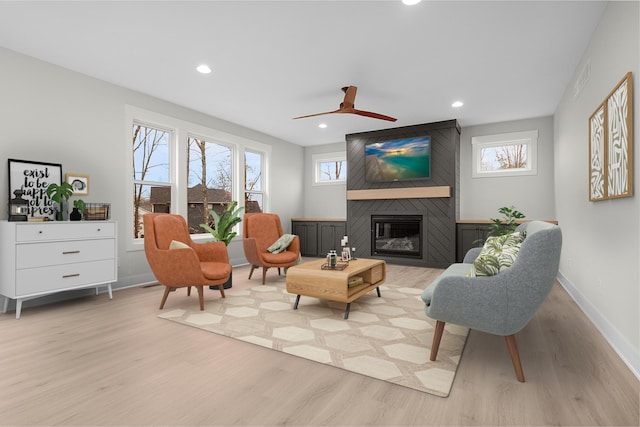 living area featuring a fireplace, light hardwood / wood-style floors, and ceiling fan