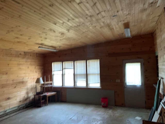 empty room with wooden ceiling, concrete flooring, and wooden walls