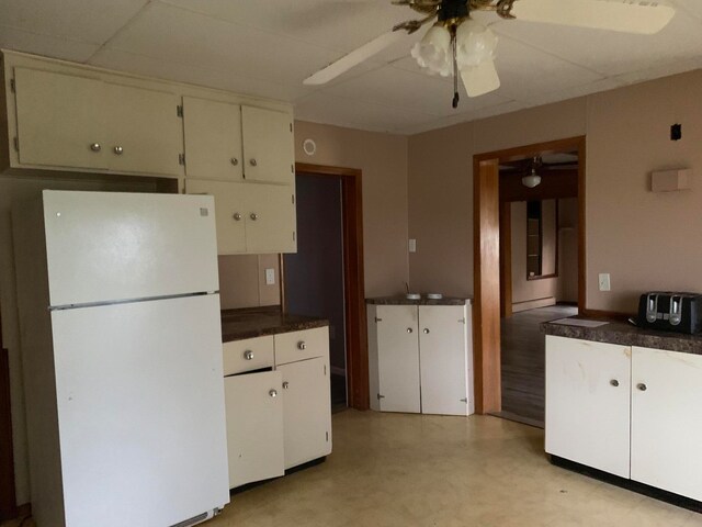 kitchen with white cabinets, white refrigerator, a baseboard heating unit, a drop ceiling, and ceiling fan