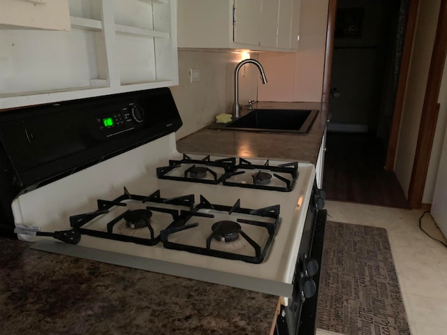 kitchen featuring light tile floors, stove, white cabinets, and sink