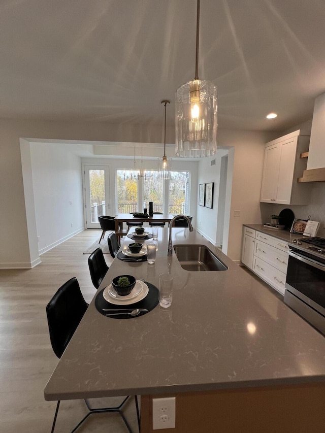 kitchen featuring sink, decorative light fixtures, light hardwood / wood-style flooring, white cabinets, and stainless steel stove