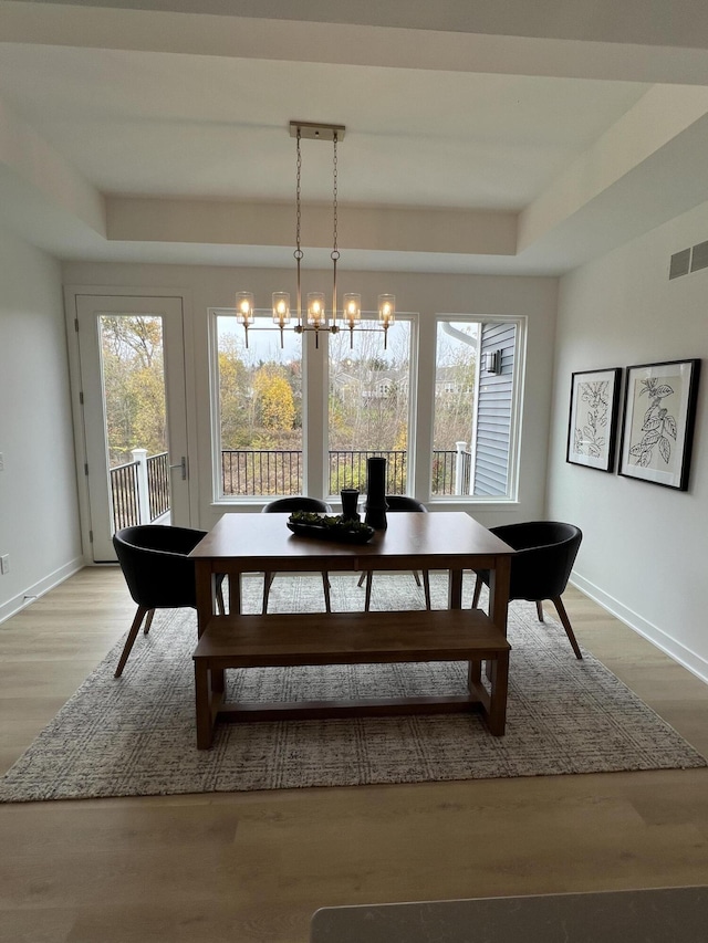 dining space with a raised ceiling, light hardwood / wood-style floors, and an inviting chandelier