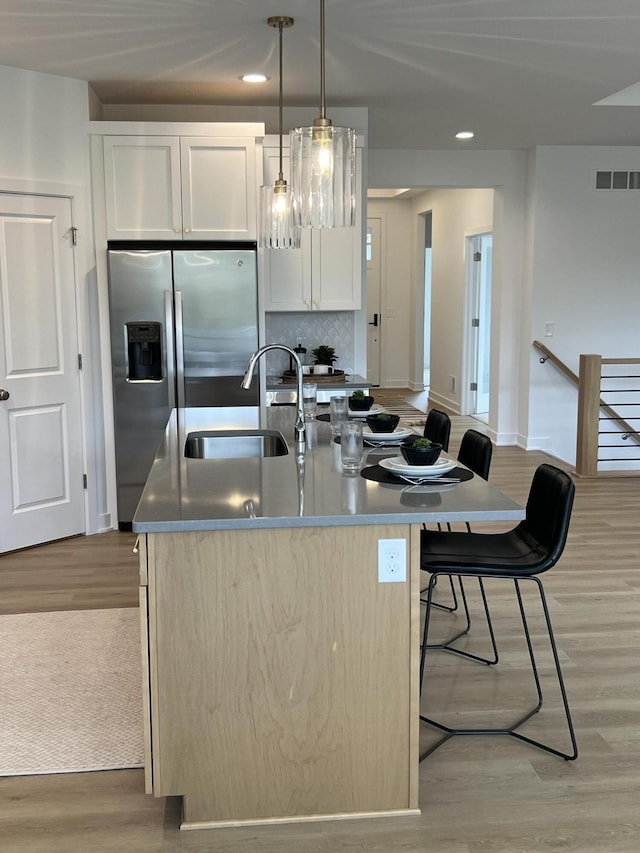 kitchen with white cabinets, decorative light fixtures, light hardwood / wood-style flooring, and a kitchen island with sink