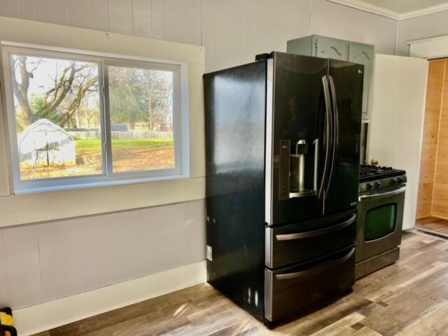 kitchen with gas stove, green cabinets, black fridge, and hardwood / wood-style flooring