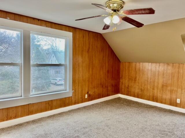 additional living space with carpet, ceiling fan, wood walls, and vaulted ceiling