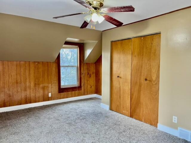 bonus room featuring carpet floors, ceiling fan, and wooden walls