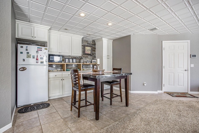 kitchen with white cabinetry, light tile patterned flooring, and white fridge