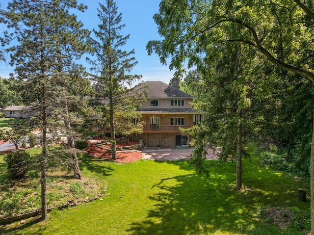 rear view of house featuring a chimney, brick siding, a lawn, and a patio area