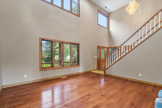 unfurnished living room with a notable chandelier, wood finished floors, visible vents, baseboards, and stairs