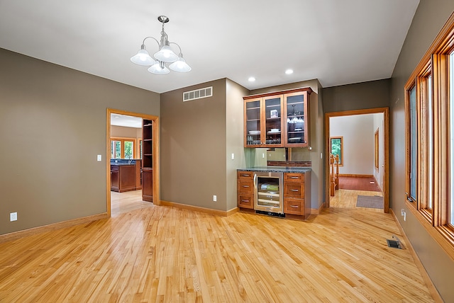 interior space with visible vents, hanging light fixtures, light wood-style flooring, glass insert cabinets, and beverage cooler