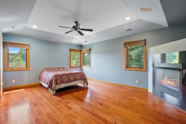 bedroom with light wood-style floors, a raised ceiling, visible vents, and multiple windows