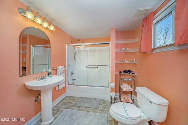 bathroom with tile floors, toilet, and shower / bath combination with glass door