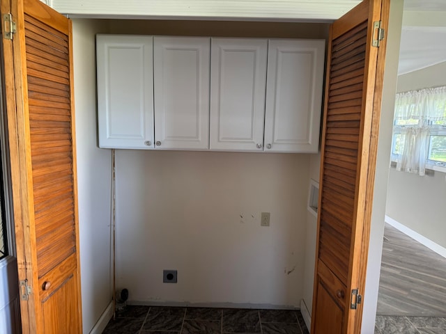 clothes washing area featuring dark tile flooring, electric dryer hookup, and cabinets