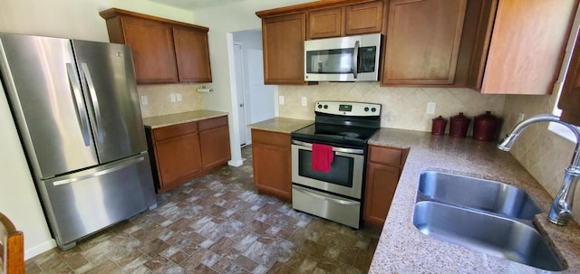 kitchen with decorative backsplash, light stone countertops, appliances with stainless steel finishes, and sink