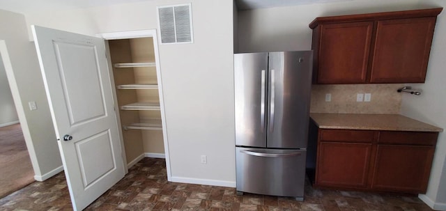 kitchen with stainless steel refrigerator, light stone counters, and backsplash