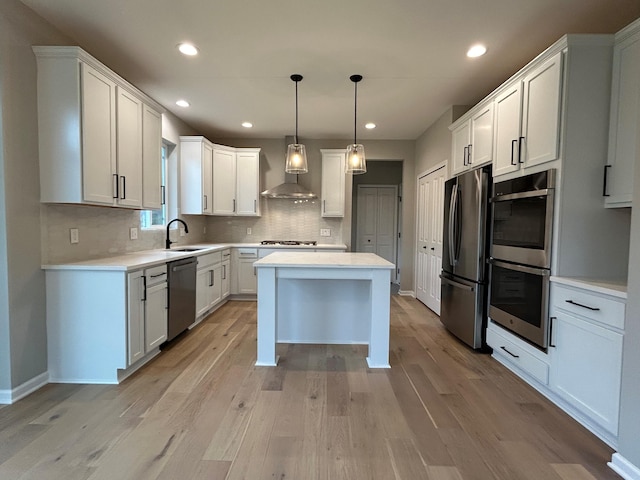 kitchen with white cabinets, wall chimney exhaust hood, light wood-type flooring, and appliances with stainless steel finishes