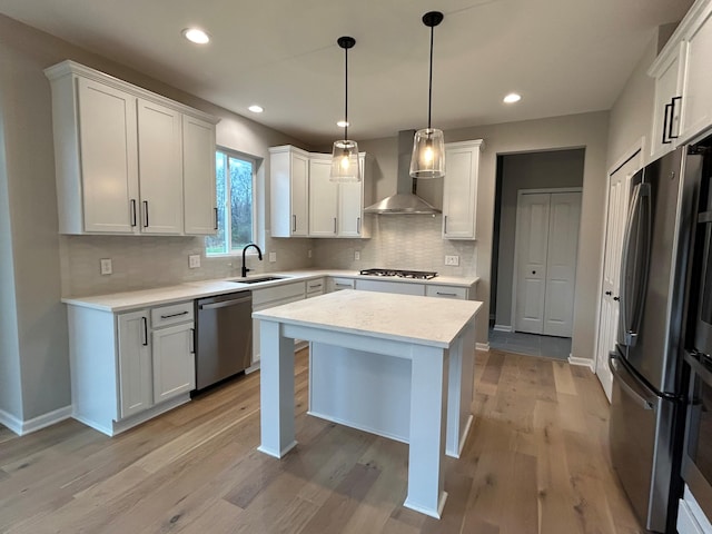 kitchen featuring wall chimney exhaust hood, stainless steel appliances, light hardwood / wood-style floors, white cabinetry, and hanging light fixtures