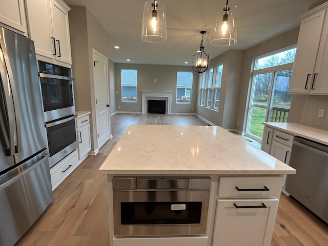 kitchen featuring light wood-type flooring, a premium fireplace, appliances with stainless steel finishes, a kitchen island, and white cabinetry