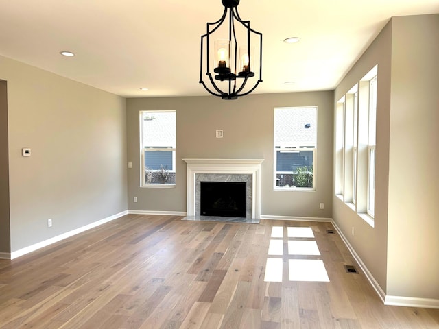 unfurnished living room featuring hardwood / wood-style flooring, a notable chandelier, a healthy amount of sunlight, and a high end fireplace