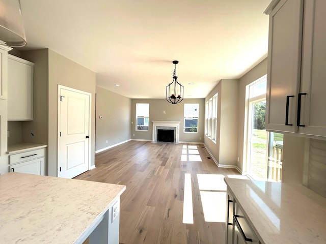 kitchen with a chandelier, light stone counters, hanging light fixtures, and light hardwood / wood-style floors