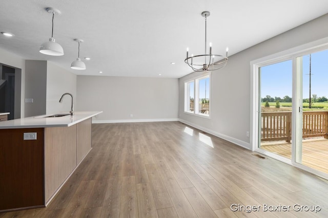 kitchen featuring sink, a chandelier, an island with sink, pendant lighting, and light hardwood / wood-style floors