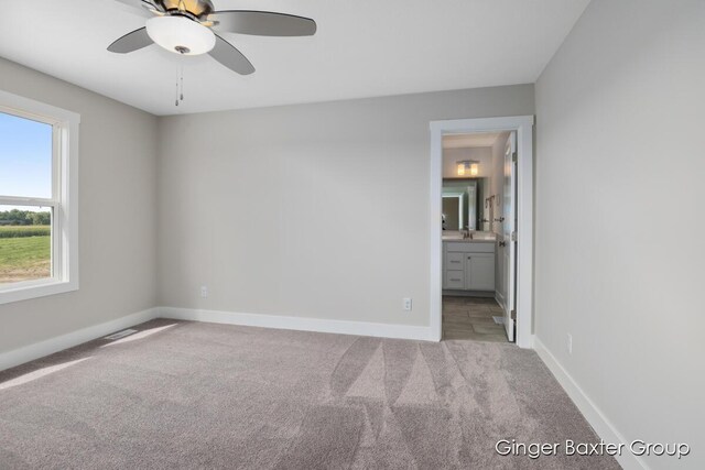 unfurnished bedroom with connected bathroom, sink, light colored carpet, and ceiling fan