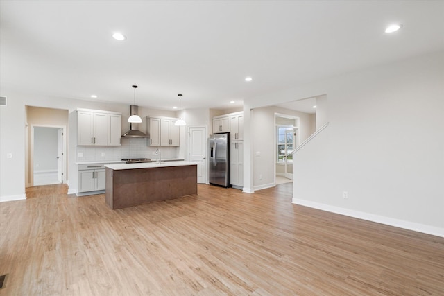 kitchen featuring light hardwood / wood-style floors, decorative backsplash, hanging light fixtures, an island with sink, and stainless steel fridge