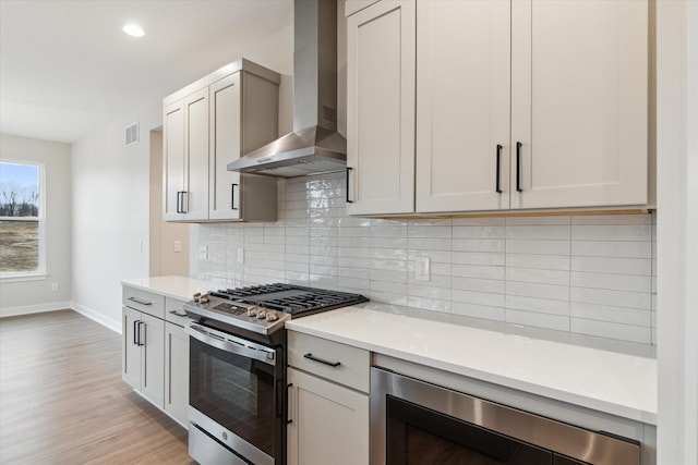 kitchen with beverage cooler, wall chimney range hood, decorative backsplash, light hardwood / wood-style flooring, and stainless steel range with gas stovetop