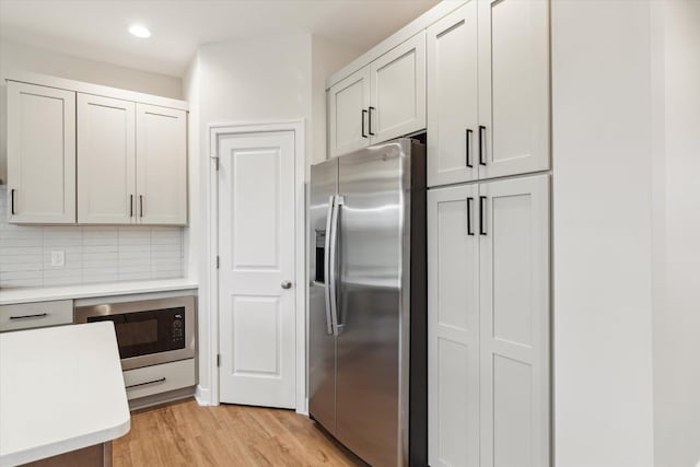 kitchen with stainless steel fridge with ice dispenser, light hardwood / wood-style flooring, decorative backsplash, black microwave, and white cabinets