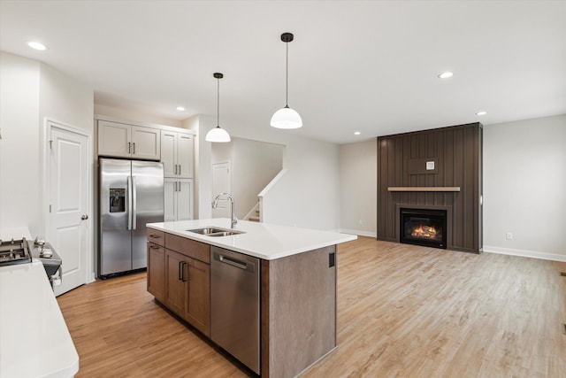 kitchen with pendant lighting, stainless steel appliances, sink, a large fireplace, and light hardwood / wood-style flooring