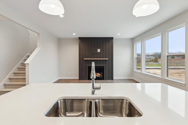 kitchen with light wood-type flooring, a large fireplace, sink, and pendant lighting