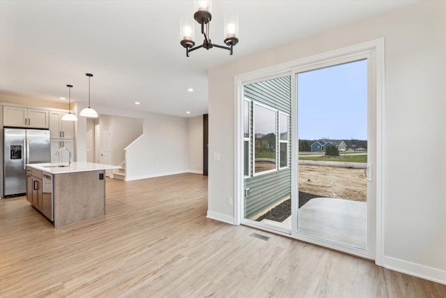 kitchen with light hardwood / wood-style flooring, stainless steel appliances, an inviting chandelier, hanging light fixtures, and a center island with sink