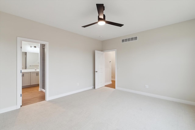 unfurnished bedroom featuring ceiling fan, light colored carpet, sink, and ensuite bathroom