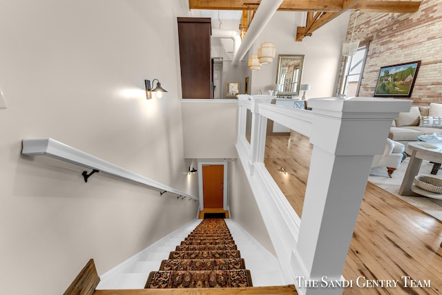 staircase featuring a towering ceiling, beamed ceiling, and hardwood / wood-style flooring