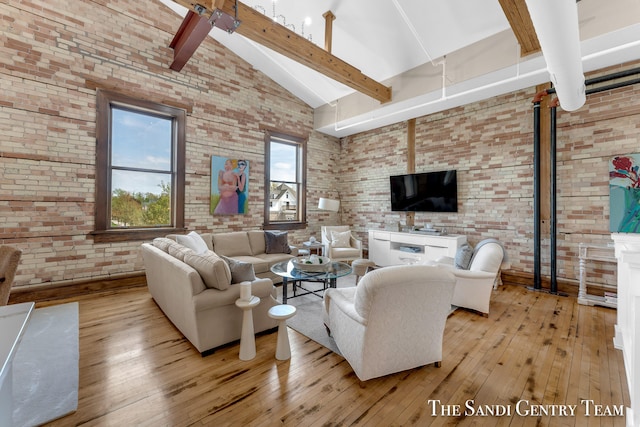 living room with light wood-type flooring, beamed ceiling, high vaulted ceiling, ceiling fan, and brick wall