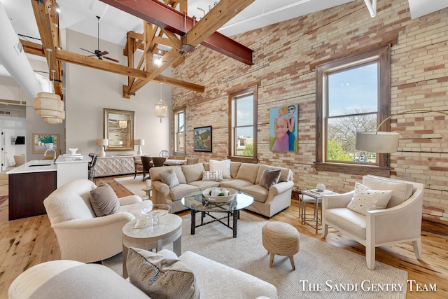 living room with light wood-type flooring, beamed ceiling, a towering ceiling, ceiling fan, and brick wall