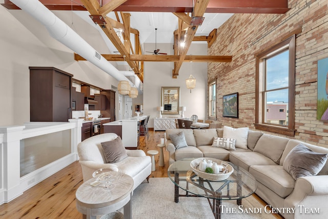 living room with light hardwood / wood-style floors, beam ceiling, a towering ceiling, ceiling fan, and brick wall