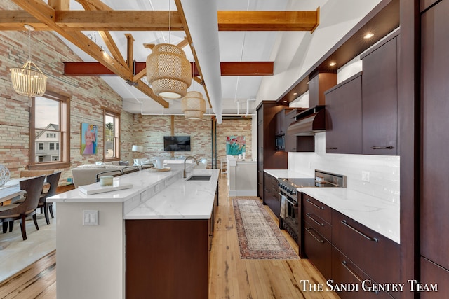 kitchen with brick wall, stainless steel stove, light wood-type flooring, a center island with sink, and sink