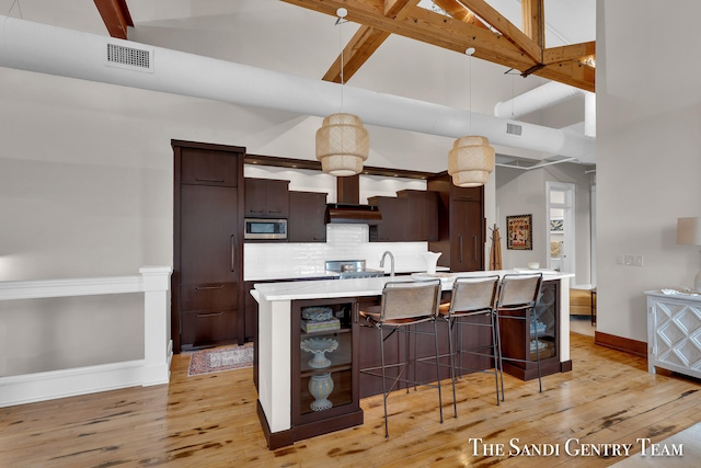 kitchen featuring light hardwood / wood-style floors, stainless steel microwave, a breakfast bar area, dark brown cabinets, and a center island with sink