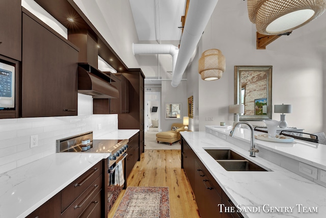 kitchen with sink, high end range, wall chimney range hood, light stone countertops, and light hardwood / wood-style floors