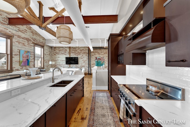 kitchen with light stone counters, brick wall, stainless steel appliances, light wood-type flooring, and sink