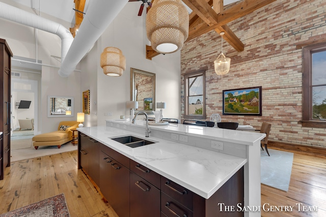 kitchen featuring a high ceiling, sink, light hardwood / wood-style flooring, and brick wall