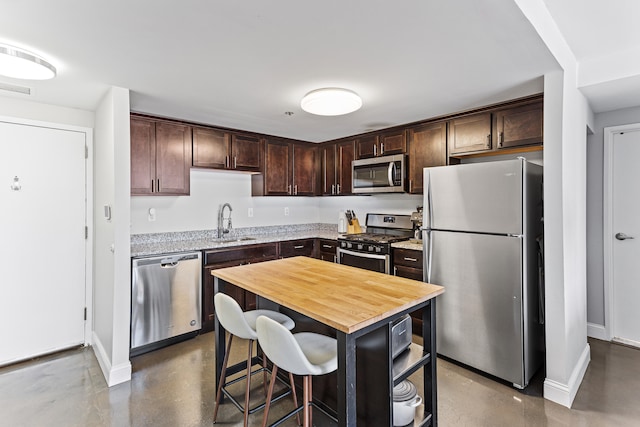 kitchen with sink, wooden counters, appliances with stainless steel finishes, a center island, and dark brown cabinetry