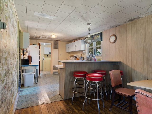 kitchen with kitchen peninsula, white cabinets, a kitchen breakfast bar, pendant lighting, and dark tile floors