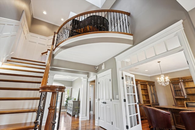 staircase featuring wood-type flooring, a towering ceiling, a notable chandelier, and ornamental molding