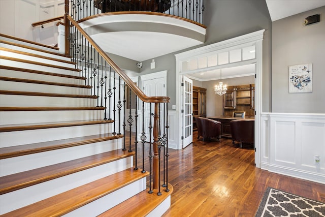 stairway featuring ornamental molding, an inviting chandelier, a towering ceiling, and hardwood / wood-style floors