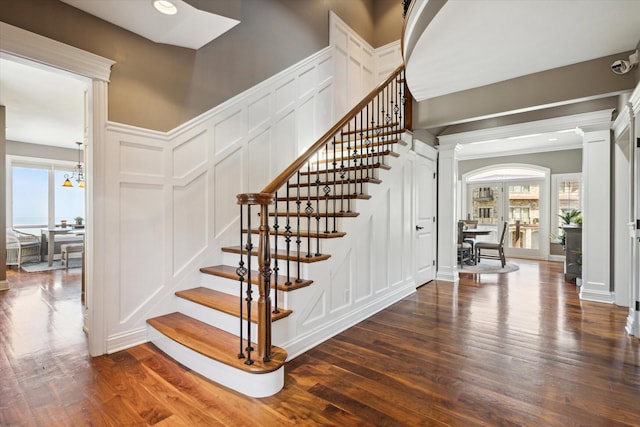 staircase featuring dark wood-type flooring, a notable chandelier, and decorative columns