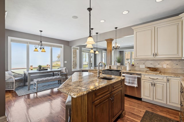 kitchen with decorative light fixtures, cream cabinetry, tasteful backsplash, dishwasher, and an island with sink